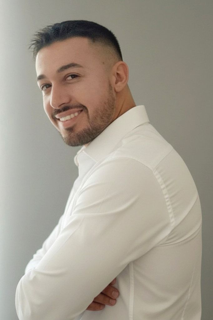 Krasimir Paunov smiling in a white shirt with arms crossed, against a light grey wall